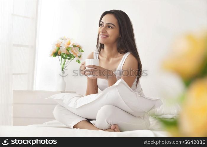 Happy young woman holding coffee cup on bed