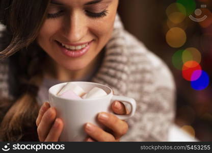 Happy young woman holding cup of hot chocolate with marshmallow