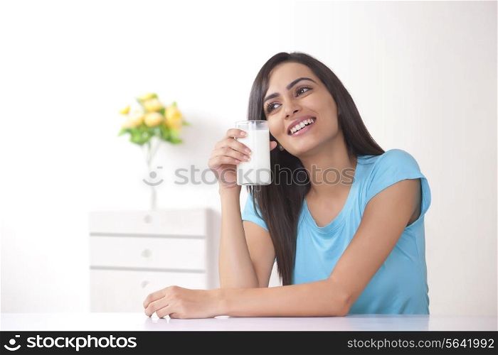 Happy young woman holding glass of milk at home
