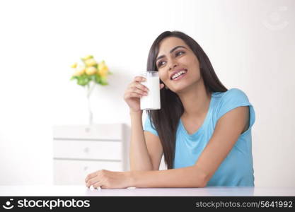 Happy young woman holding glass of milk at home