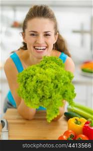Happy young woman holding green salad in kitchen