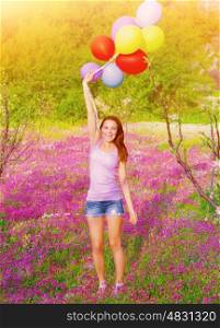 Happy young woman holding in hands many colorful balloons, having fun on purple floral field, summer time season, freedom concept