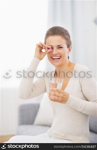 Happy young woman holding pill and glass of water