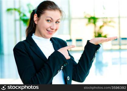Happy young woman holding something on the palm of your hand and points a finger at her