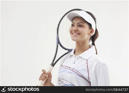 Happy young woman holding tennis racket while looking away isolated over gray background