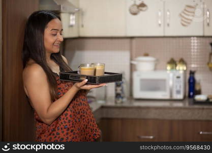 Happy young woman holding tray with coffee in the kitchen