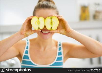 Happy young woman holding two slices of apple in front of eyes