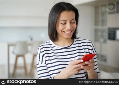 Happy young woman holds smartphone, chatting in social network, reading good news, shopping via online store app. Smiling female enjoy web surfing information, learning foreign language at home.. Happy female hold phone chat in social network read good news, shopping via online store app at home