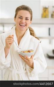 Happy young woman in bathrobe eating healthy breakfast
