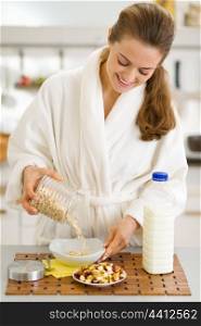 Happy young woman in bathrobe putting oatmeal into plate