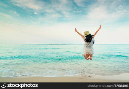 Happy young woman in casual style fashion and straw hat jumping at sand beach. Relaxing, fun, and enjoy holiday at tropical paradise beach with blue sky and white clouds. Girl in summer vacation.