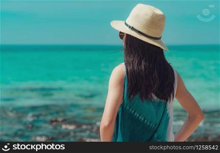 Happy young woman in casual style fashion and straw hat standing at sea beach. Relaxing and enjoy holiday at tropical paradise beach with emerald green water. Girl in summer vacation. Summer vibes.