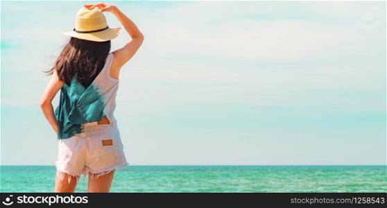 Happy young woman in casual style fashion and straw hat standing at sea beach. Relaxing and enjoy holiday at tropical paradise beach with emerald green sea water. Girl in summer vacation. Blue sky.