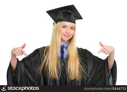 Happy young woman in graduation gown pointing down on copy space