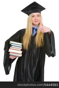 Happy young woman in graduation gown showing books and thumbs up