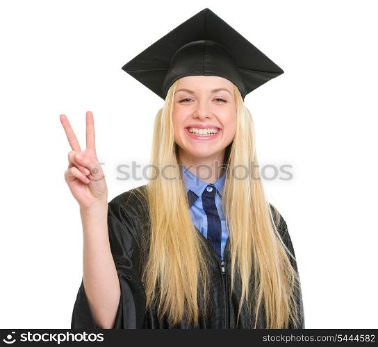 Happy young woman in graduation gown showing victory gesture