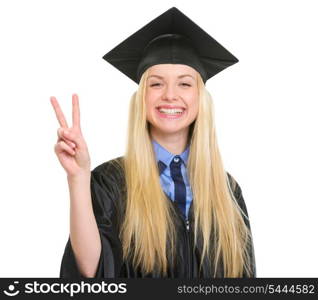 Happy young woman in graduation gown showing victory gesture
