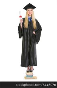 Happy young woman in graduation gown with diploma standing on stack of books