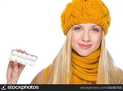 Happy young woman in hat and scarf showing pack of pills
