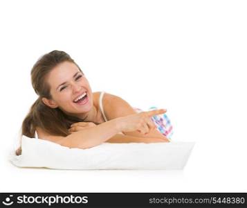 Happy young woman in pajamas laying on pillow and pointing on copy space