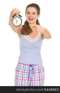 Happy young woman in pajamas pointing on alarm clock