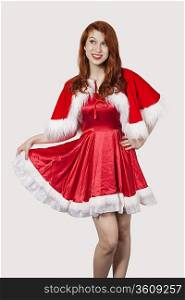 Happy young woman in Santa costume standing against gray background