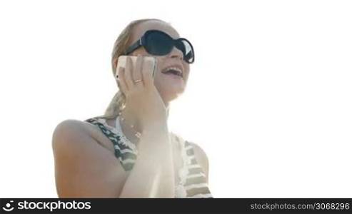Happy young woman in sunglasses talking on the phone and sun shines behind her back.