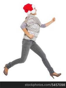 Happy young woman in sweater and christmas hat running sideways