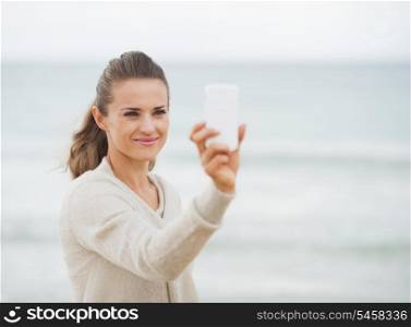 Happy young woman in sweater on beach taking photo using cell phone