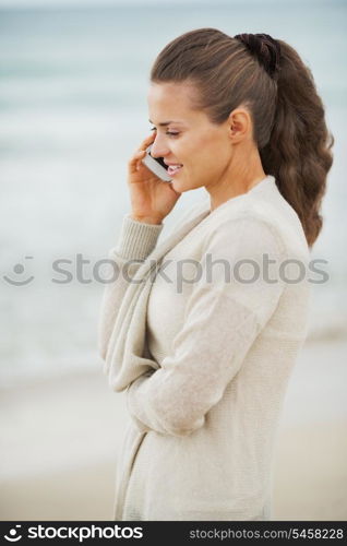 Happy young woman in sweater on beach talking mobile phone
