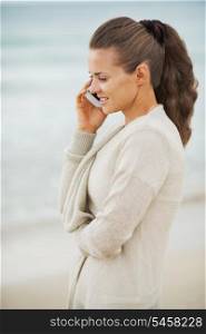 Happy young woman in sweater on beach talking mobile phone