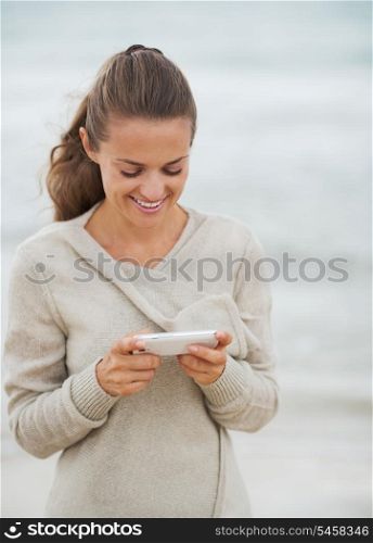 Happy young woman in sweater on beach writing sms