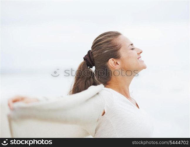 Happy young woman in sweater on lonely beach rejoicing