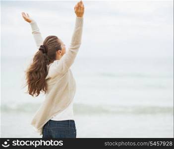 Happy young woman in sweater rejoicing on beach . rear view