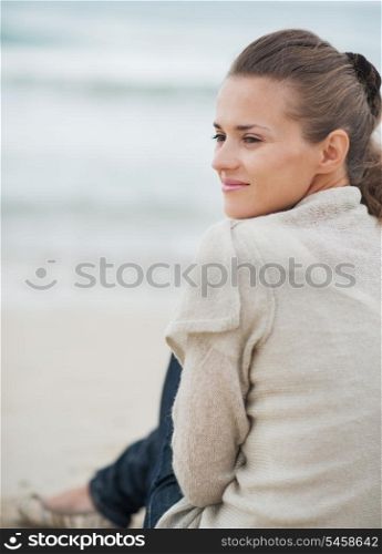 Happy young woman in sweater sitting on lonely beach