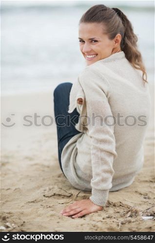 Happy young woman in sweater sitting on lonely beach