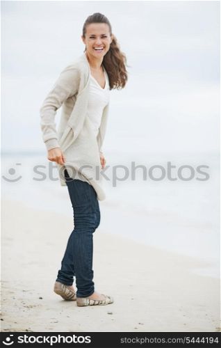 Happy young woman in sweater walking on lonely beach