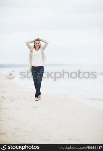 Happy young woman in sweater walking on lonely beach