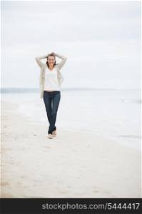 Happy young woman in sweater walking on lonely beach