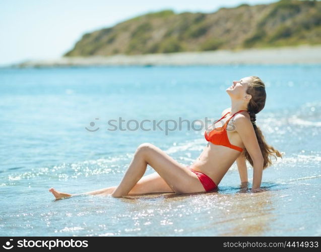 Happy young woman in swim suite laying on sea shore