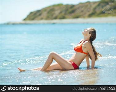 Happy young woman in swim suite laying on sea shore