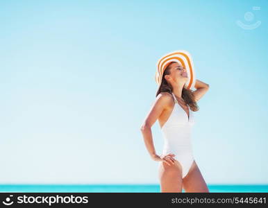 Happy young woman in swimsuit and beach hat relaxing on beach