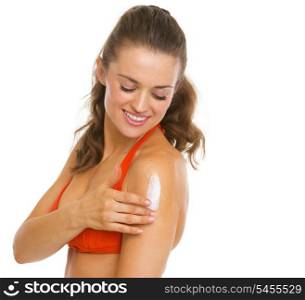 Happy young woman in swimsuit applying sun block creme