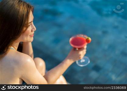 happy young woman in swimsuit enjoying with a fresh cocktail at poolside of the swimming pool