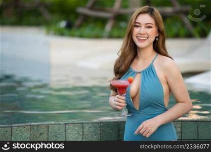 happy young woman in swimsuit enjoying with a fresh cocktail near the swimming pool