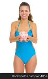 Happy young woman in swimsuit giving piggy bank