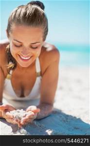 Happy young woman in swimsuit laying on beach and playing with sand