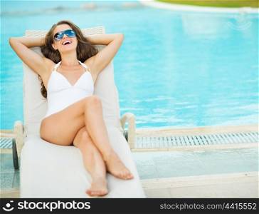 Happy young woman in swimsuit laying on chaise-longue poolside