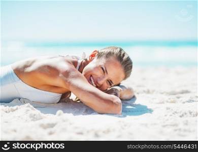 Happy young woman in swimsuit laying on sandy beach