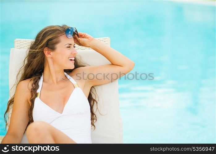 Happy young woman in swimsuit on chaise-longue and looking on copy space